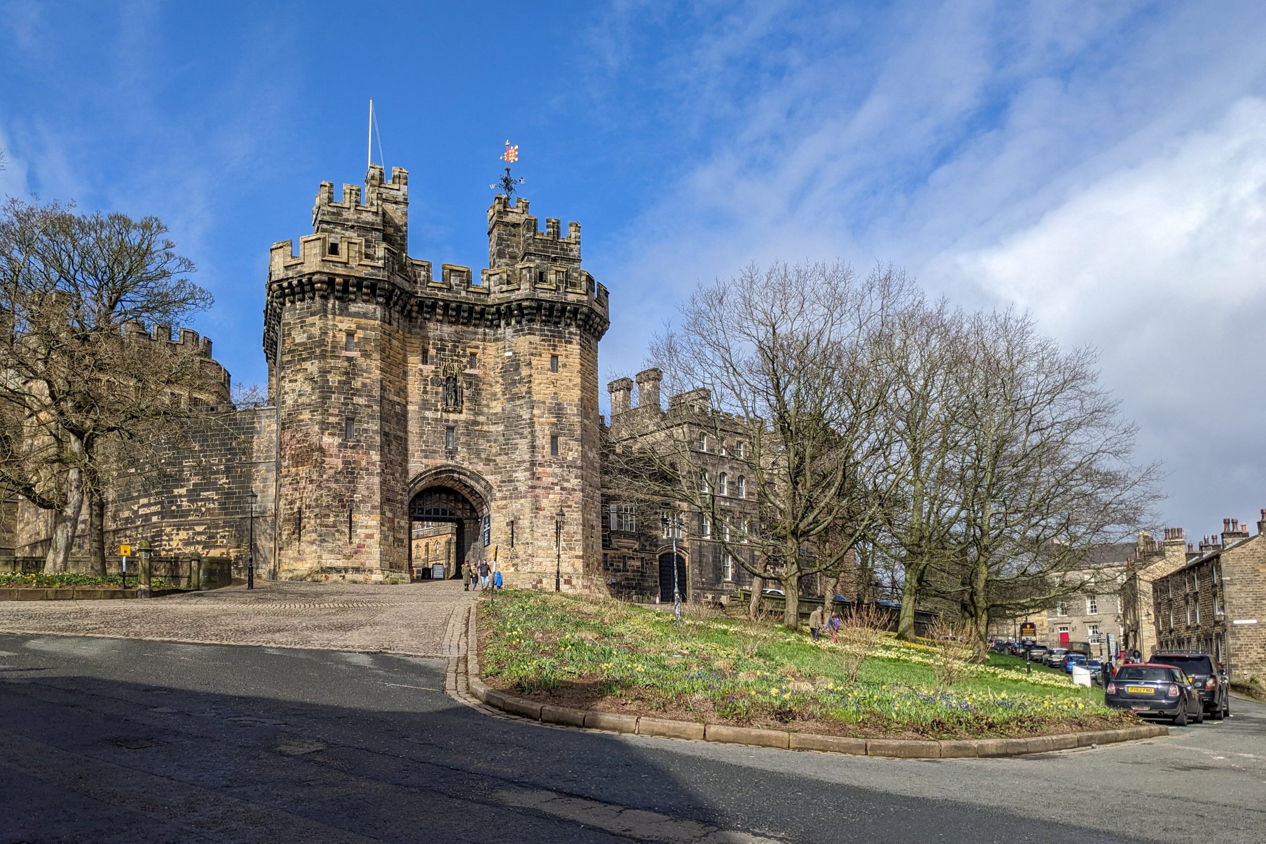 Stone fortress gate with battlements and arched entrance, blue sky behind and leafless trees nearby.
